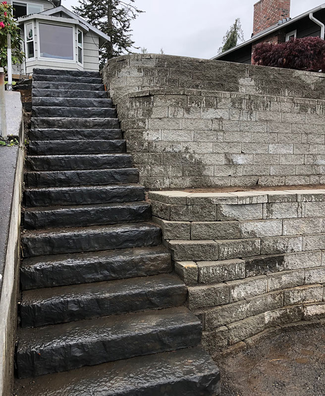 Steep stone steps with railing and terraced block retaining wall